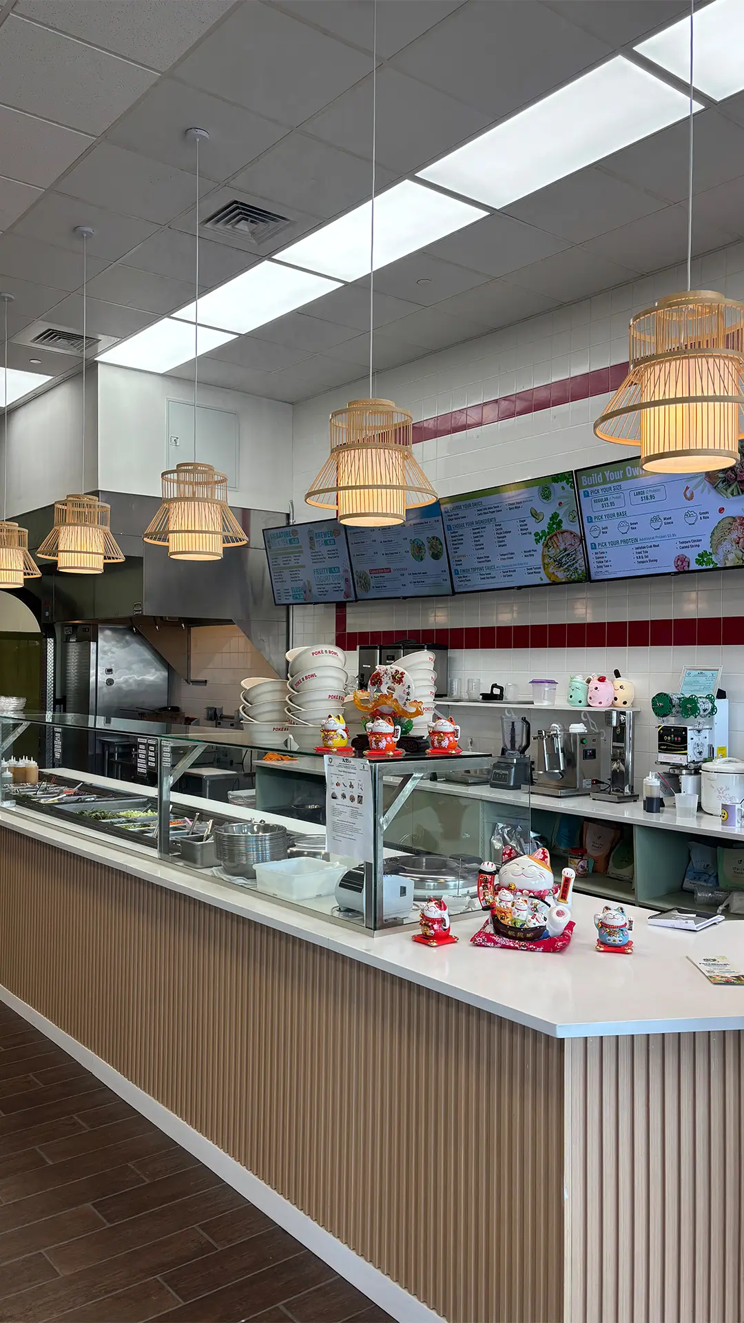 Modern poke restaurant counter with bamboo pendant lights, digital menu boards, and lucky cat figurines on the service bar.